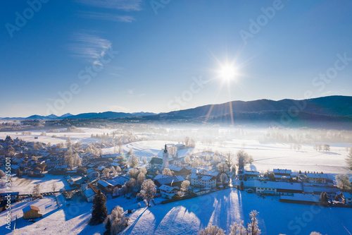 Germany, Bavaria, Reichersbeuern, Drone view of sun shining over snow-covered village