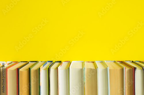 An even row of books close up on a bright yellow background and copy space