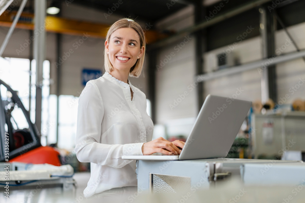 Smiling young woman using laptop in a factory