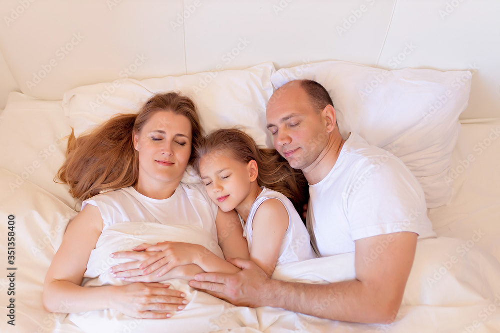 Happy family, mom, dad, daughter sleep in bed in the bedroom at home Happy family, mom, dad, daughter sleep in bed in the bedroom at home