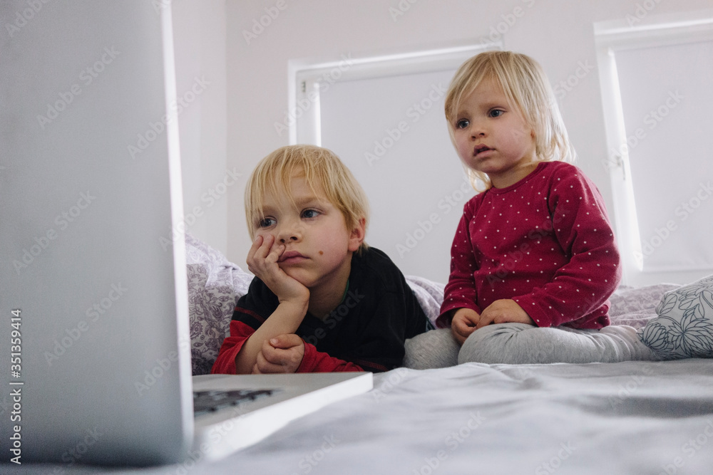Portrait of little girl and her older brother on bed looking at laptop Portrait of little girl and her older brother on bed looking at laptop