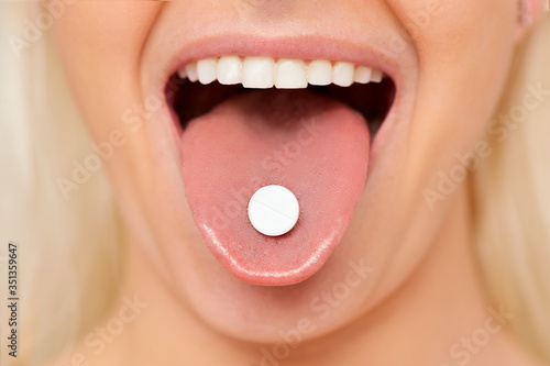 Beautiful woman mouth with pill on tongue. Girl taking medicine