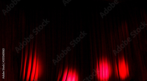 Panorama of closed red theater curtains and backstage scene. Four red circles of light in the dark at time of entertainment show. Small depth of view.