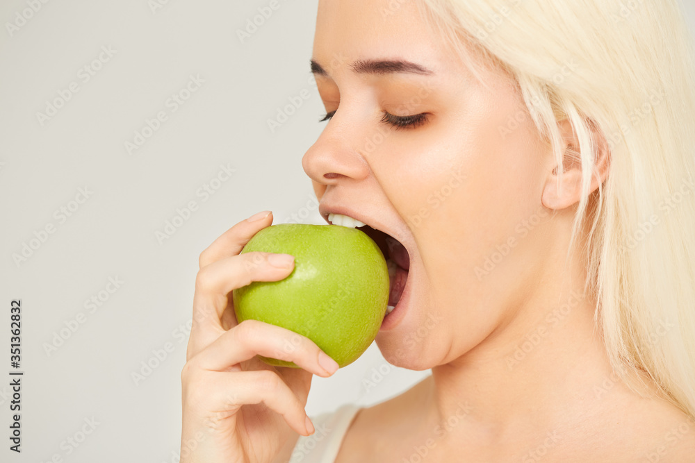 Woman with Apple. Beautiful girl closeup eating an apple on a gray background, healthy teeth. High Resolution Image Woman with Apple. Beautiful girl closeup eating an apple on a gray background, healthy teeth. High Resolution Image