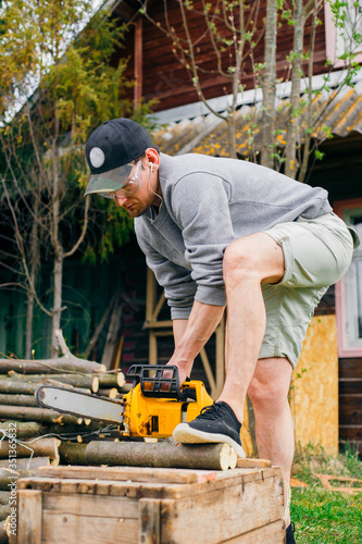 Caucasian young man while working with wood, wearing technical glasses. He used chainsaw.