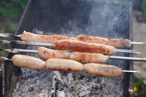 Close up of toasted sausages on skewers. Succulent kupaty roasting on chargrill. Concept of picnic outdoor.