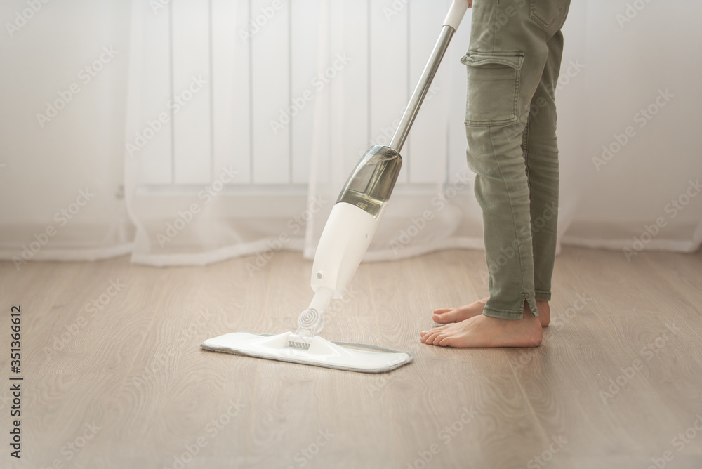 Fototapeta premium a child in green pants mops the floor in a bright apartment