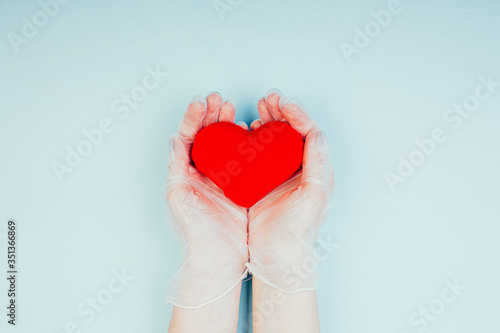 Female hands in medical gloves hold a red heart. Pandemic Health Care Concept for Doctors