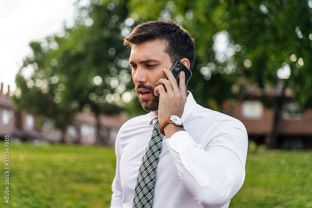 Young business man with white shirt and tie in outdoor park making phone call Young business man with white shirt and tie in outdoor park making phone call