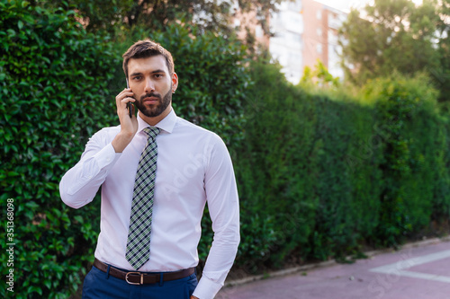 Young business man with white shirt and tie in outdoor park making phone call