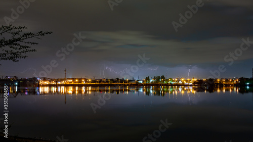 Night city during a thunderstorm on the horizon. River, sky, lightning over the city. Horizontal orientation.