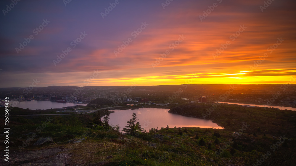 Obraz premium Vibrant sunset over St John's Newfoundland, seen from the top of Signal Hill overlook. Colorful clouds and reflections in the harbour. 