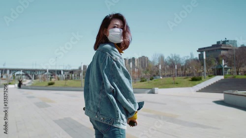 Back view of young woman in a jeans jacket rides the scooter in a summer park photo