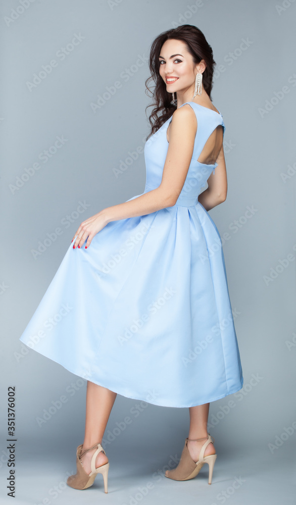 Portrait of beautiful young european brunette girl in light blue dress on grey background