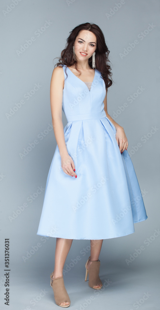 Portrait of beautiful young european brunette girl in light blue dress on grey background