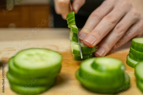 Women's hands cut a fresh cucumber into sticks on a wooden Board close up