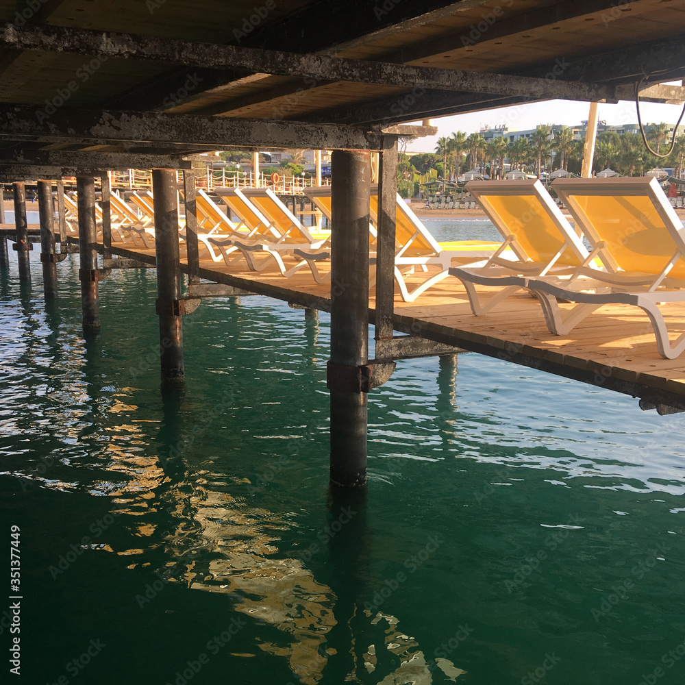 Yellow deck chairs with umbrellas on the pier, photo taken early in the morning at sea in Turkey during sunrise. Mobile photography and selective focus.