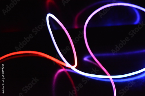 Red and blue light wire, a light guide wire with different light transmission, light spectrum, and light effects located in a chaotic state with light reflection on a black glossy background.