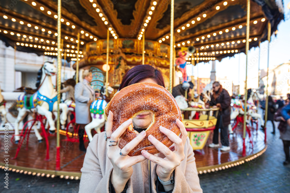A sugary donut in front of an ancient German Horse Carousel built in 1896 in Navona Square, Rome, Italy