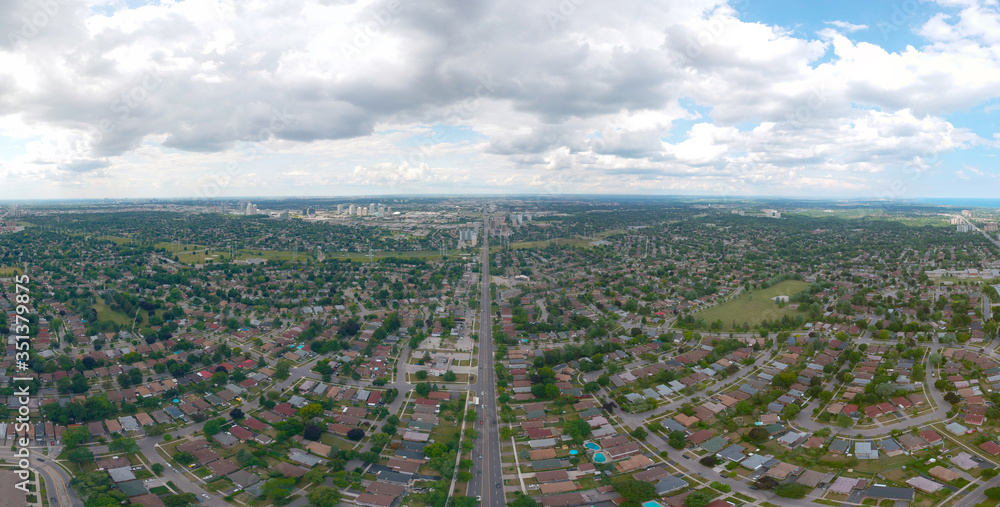 Artistic view of Toronto city at cloudy sky day. Panoramic summer landscape in  Ontario, Canada. North American urban commuter background of houses, stores, parking, and roads with green trees.