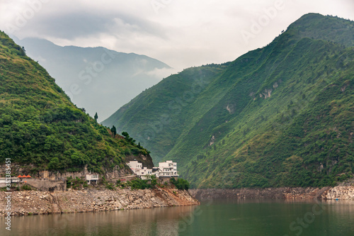 Guandukou, Hubei, China - May 7, 2010: Wu Gorge in Yangtze River. White buildings built on edge of green water in bend in canyon of green mountains and cloudscape. photo