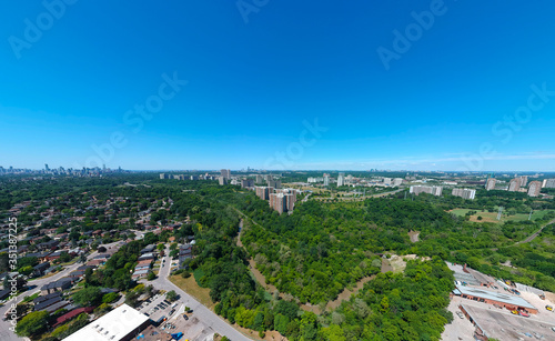 Sunny summer day with plain blue sky and panoramic city landscape in Toronto, Ontario, Canada from urban industrial area to the residencies. Factories, houses, stores, parks, roads with green trees.