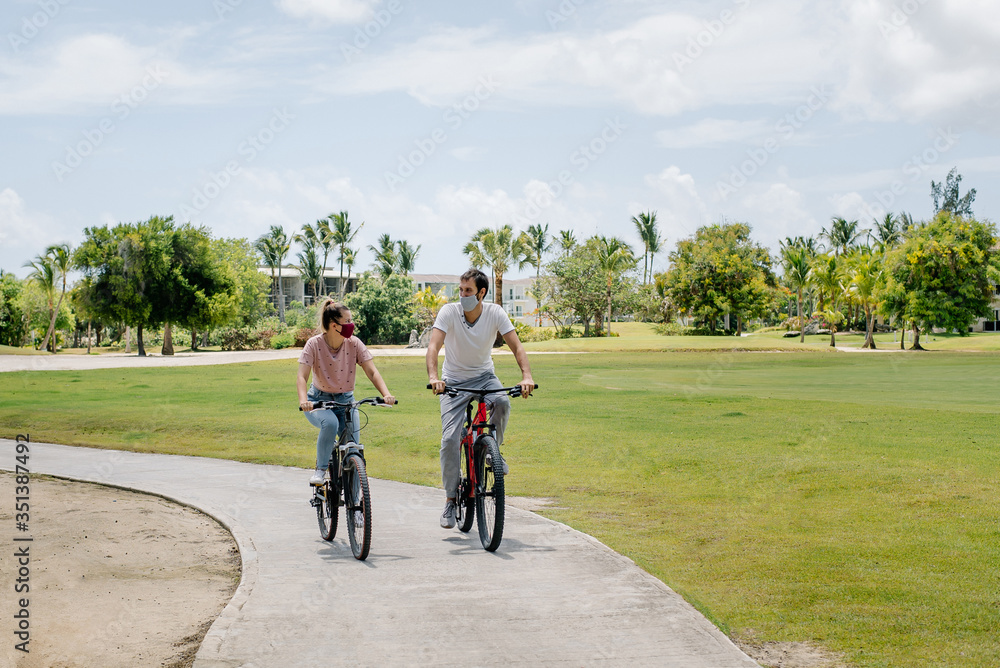 Obraz premium 2 cyclists (woman and man) ride a bike in the park. They wear protective masks against coronavirus covid-19