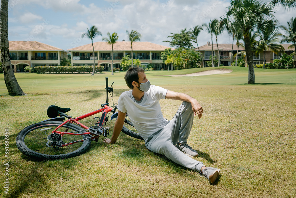 Fototapeta premium a man cyclist with a beard and a mask. mask against the virus coronavirus codiv-19. in a white tank top on a bike.