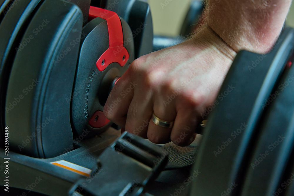 Hand gripping adjustable dumbbells for working out at home. male hand with ring visible. Hand gripping adjustable dumbbells for working out at home. male hand with ring visible.