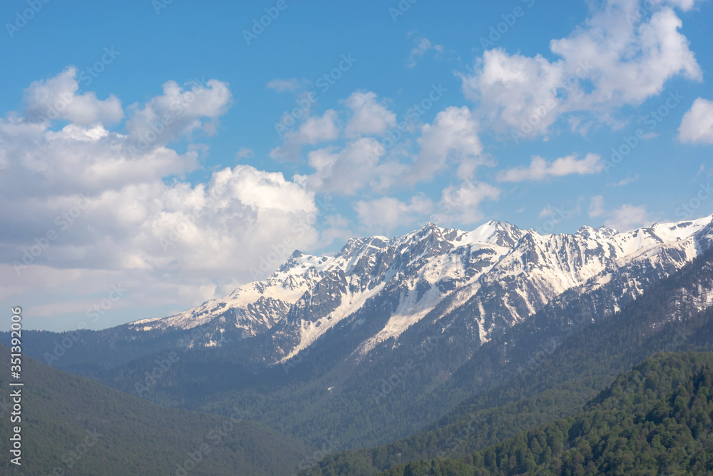Snow-capped mountains and clouds. Spring landscape with mountains and forest. Rosa Khutor ski resort Sochi Krasnodar territory. Snow in April in the Caucasus mountains.