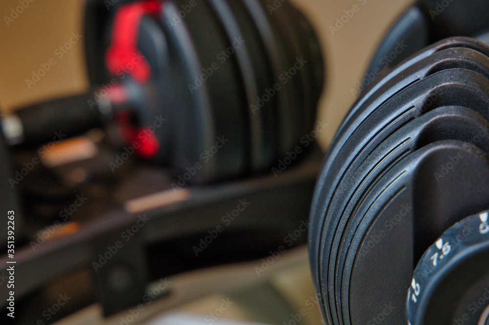 Set of dumbbells sitting on rack. Adjustable weights on stand with tan or yellow background