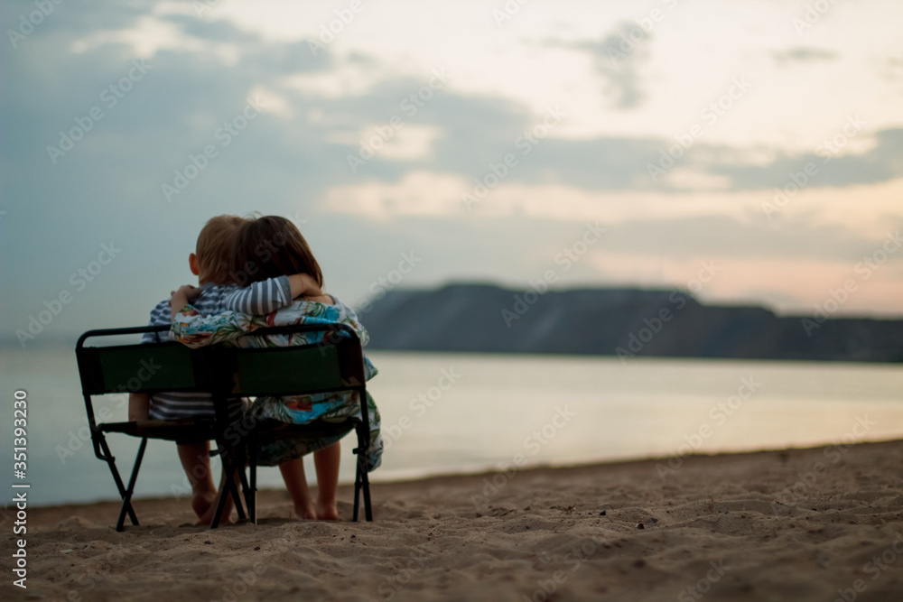Fototapeta premium a boy and a girl sit on chairs on the beach in the evening