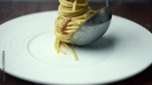 Preparing and decorating spaghetti/pasta with a ladle from a pan full with spaghetti carbonara into a serving white plate