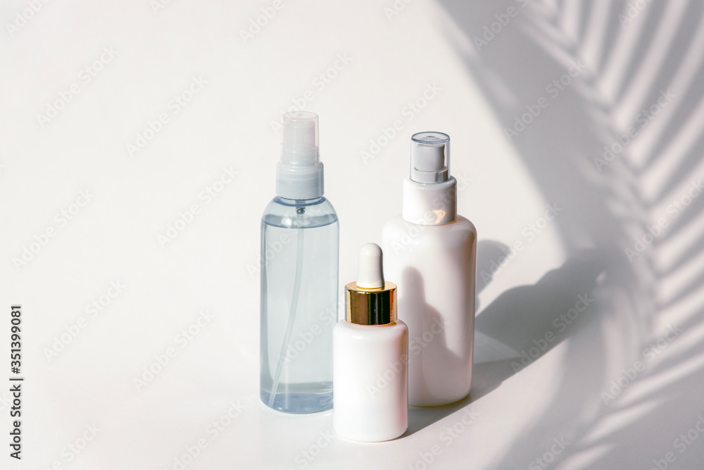 Cosmetic tonic, serum and micellar water in blank packages on a background of white wall with palm leaves shadows. Natural skincare products concept. Cosmetic tonic, serum and micellar water in blank packages on a background of white wall with palm leaves shadows. Natural skincare products concept.