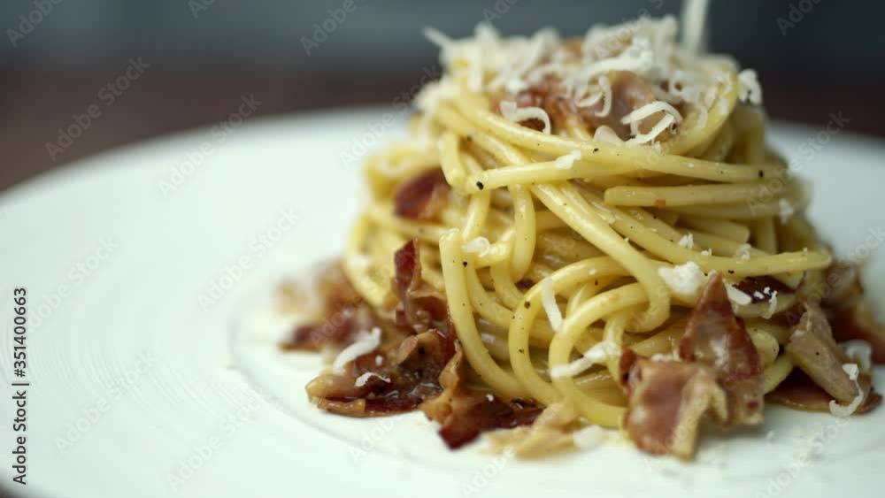 Close-up of adding cheese on top of fresh-made Spaghetti/pasta Carbonara with pancetta in a white serving plate. Close-up of adding cheese on top of fresh-made Spaghetti/pasta Carbonara with pancetta in a white serving plate.