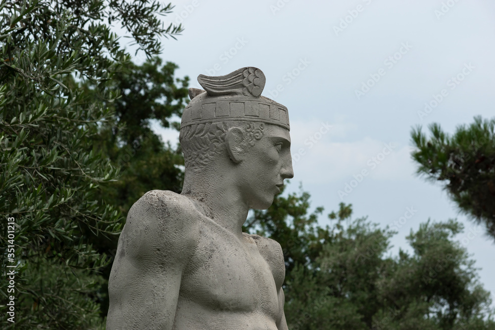 Fragment of a marble statue of Perseus in the landscape park of the Aivazovsky sanatorium in Partenit in Crimea against the backdrop of evergreen and flowering shrubs.