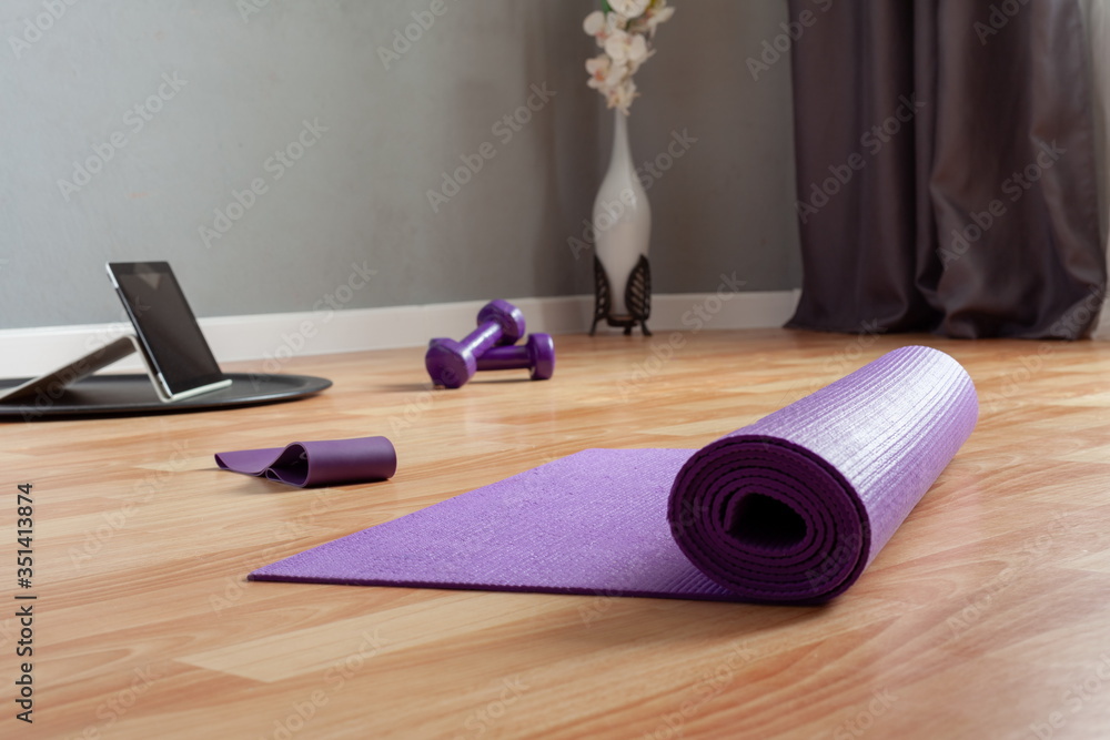 Obraz premium sports equipment and a tablet computer are laid out on the floor in a room. Home workouts at home using a mat, dumbbell, stretch marks. Home online fitness
