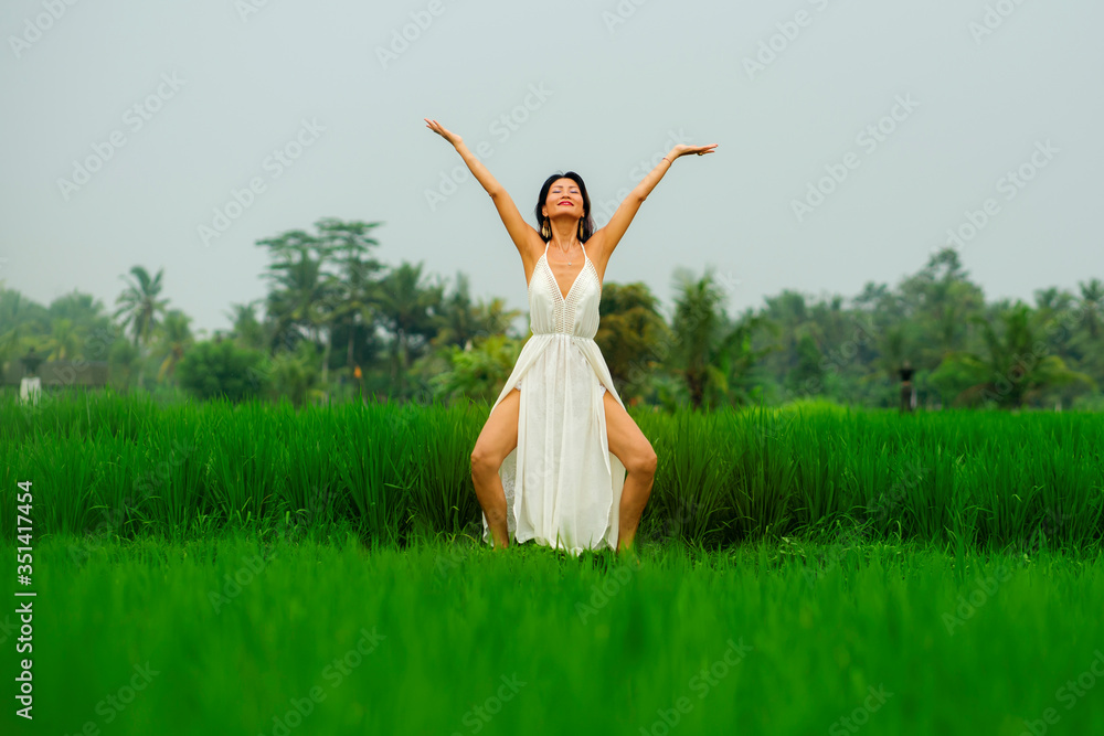 body and mind connection with nature - happy and beautiful Asian Japanese woman doing yoga and meditation exercise outdoors at idyllic green rice field enjoying tropical holidays