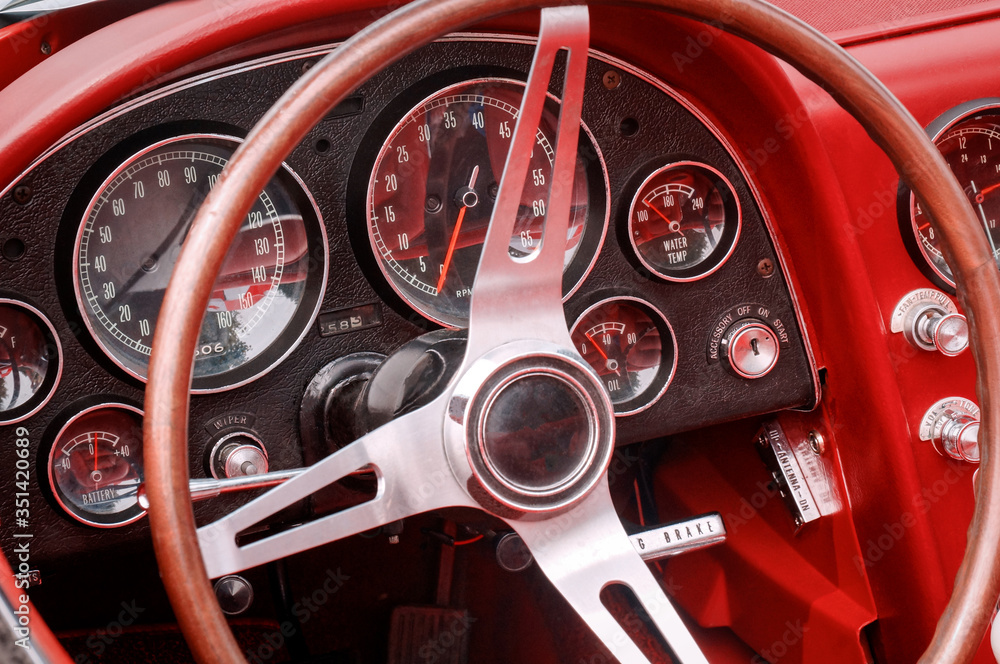 Part of interior with steering wheel, speedometer, revs, fuel, oil, water temperature and battery dials and knobs on the front panel of red oldtimer sports car Part of interior with steering wheel, speedometer, revs, fuel, oil, water temperature and battery dials and knobs on the front panel of red oldtimer sports car