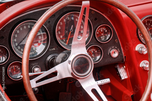 Part of interior with steering wheel, speedometer, revs, fuel, oil, water temperature and battery dials and knobs on the front panel of red oldtimer sports car © Vadim Rodnev