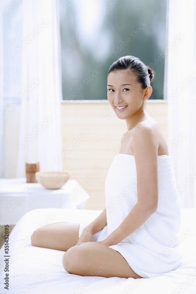 Woman wrapped in towel sitting on massage table Woman wrapped in towel sitting on massage table