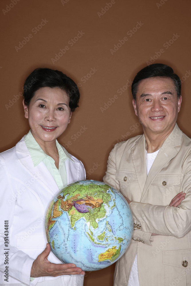 Senior woman holding globe, senior man posing with arms folded Senior woman holding globe, senior man posing with arms folded