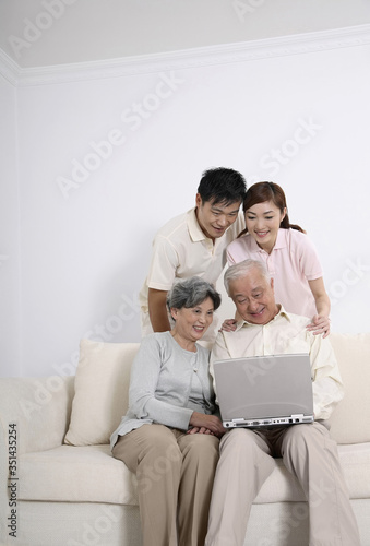 Senior man using laptop while senior woman, woman and man watches him