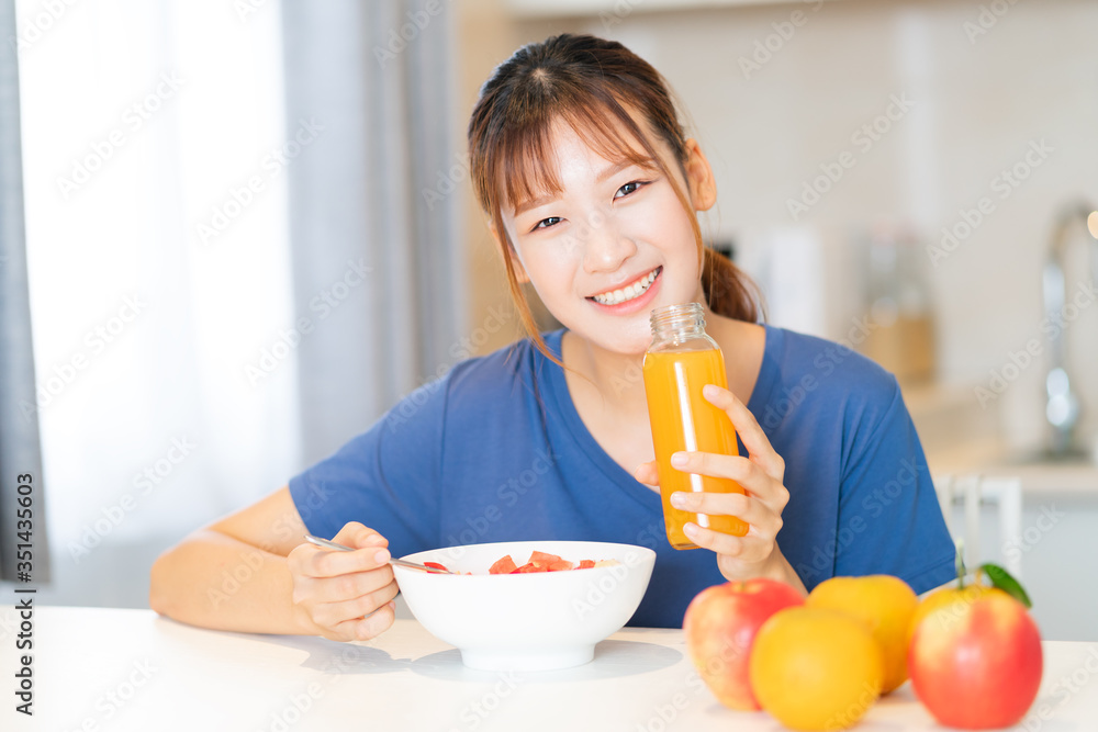 A young Asian woman eating breakfast with fruit in her kitchen A young Asian woman eating breakfast with fruit in her kitchen