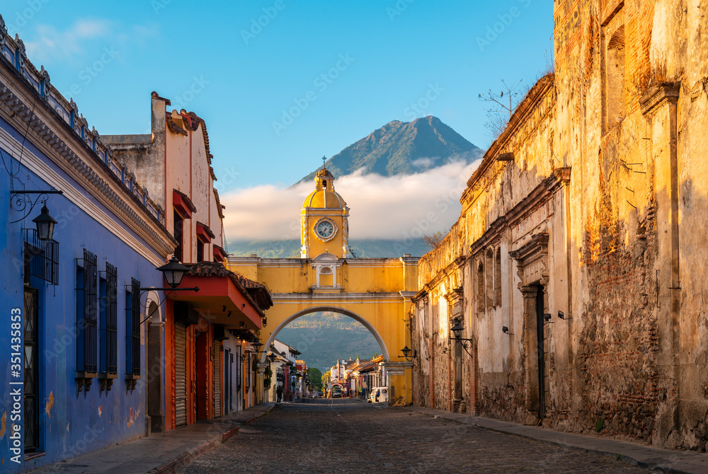 The Santa Catalina Arch in the Main Street of Antigua City without people and the Agua Volcano in the background at sunrise, Guatemala.