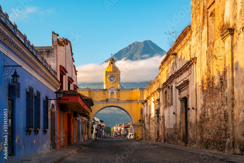The Santa Catalina Arch in the Main Street of Antigua City without people and the Agua Volcano in the background at sunrise, Guatemala.