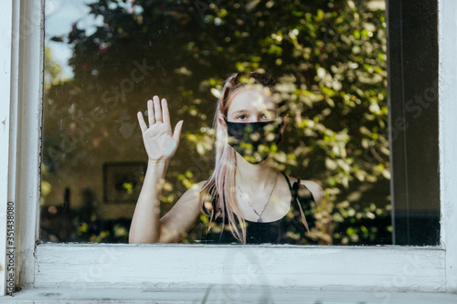 Girl wearing a mask staring out the window during a lockdown