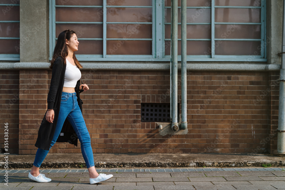 Side view of stylish young Asian woman walking at metal wall. stock photo