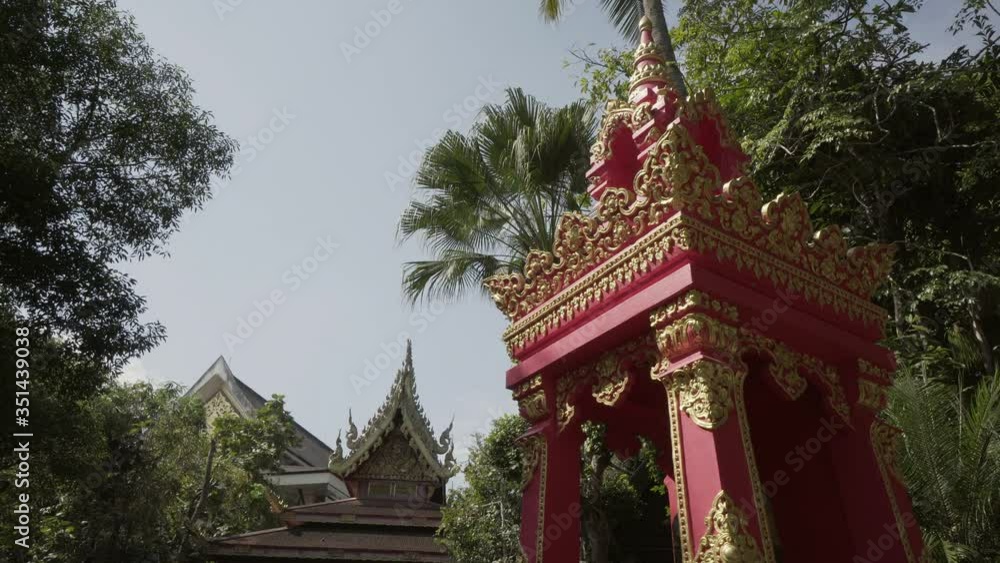 Panning shot of gold carving on red structure by tourists at entrance against trees on sunny day - Chiang Rai, Thailand Panning shot of gold carving on red structure by tourists at entrance against trees on sunny day - Chiang Rai, Thailand