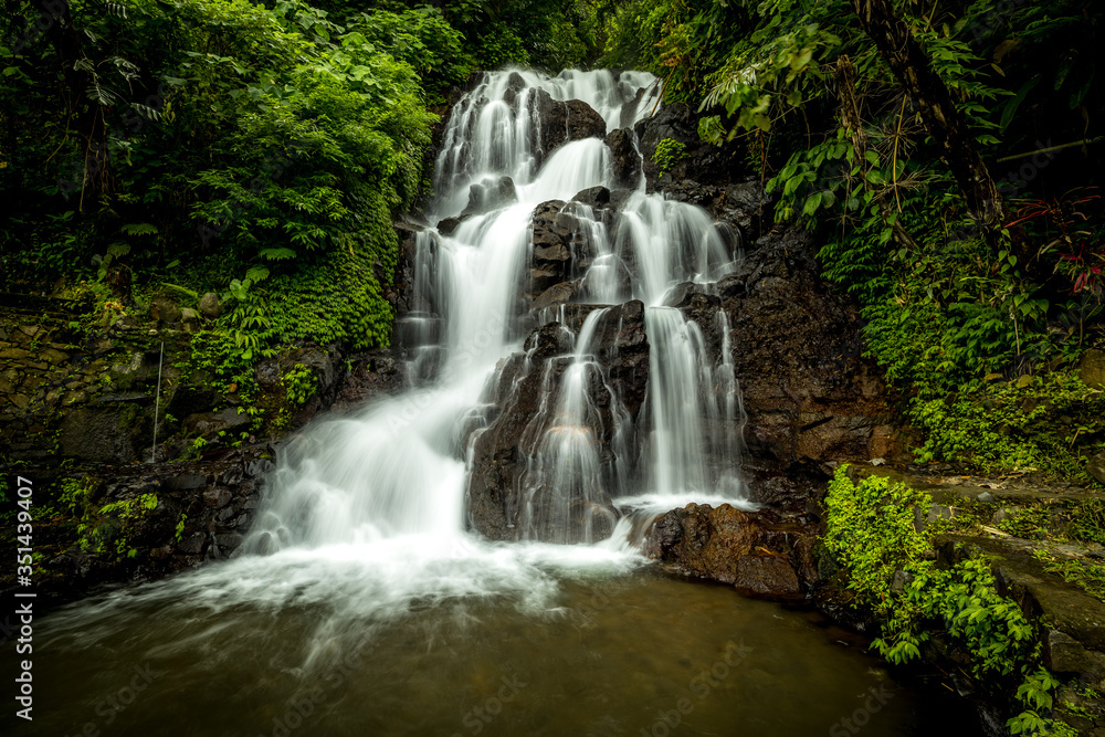 Obraz premium Waterfall landscape. Beautiful hidden Jembong waterfall in tropical rainforest in Ambengan, Bali. Slow shutter speed, motion photography.